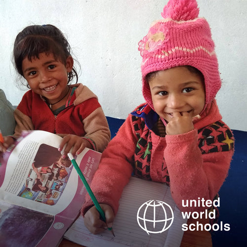 Two school children are sat smiling. One is holding a pencil in one hand and writing on lined paper. At the right of the image is the United World schools logo.